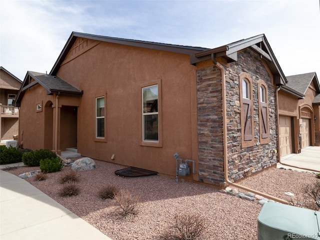 view of side of property with a garage, stone siding, concrete driveway, and stucco siding