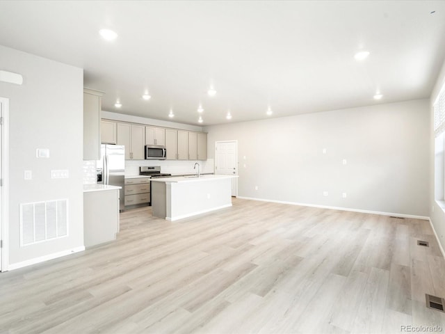 kitchen with a center island with sink, visible vents, stainless steel appliances, light countertops, and a sink