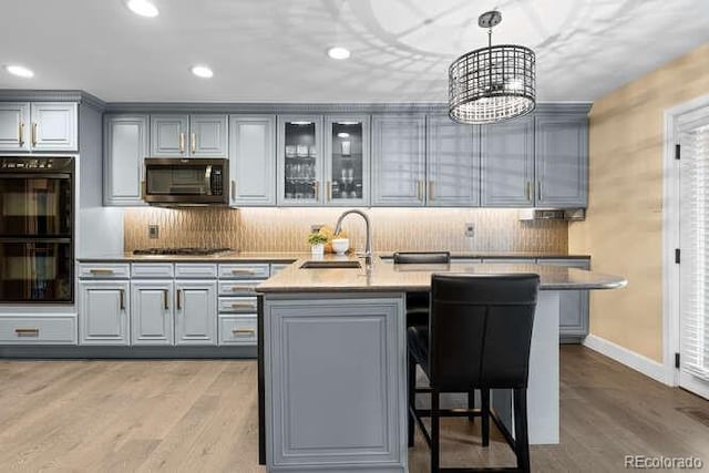 kitchen with gray cabinets, a kitchen island with sink, sink, and black double oven