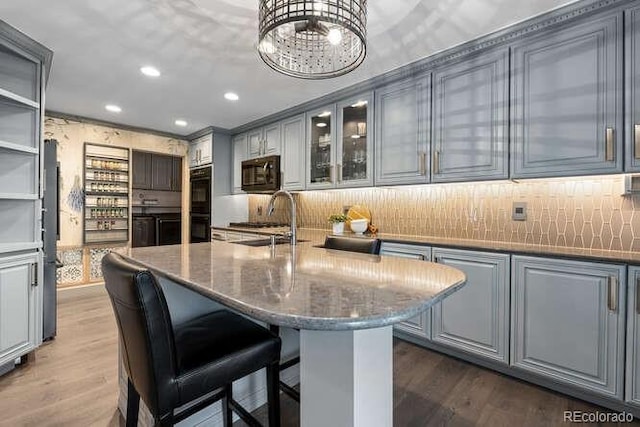 kitchen featuring sink, dark stone countertops, gray cabinets, a kitchen island with sink, and black appliances