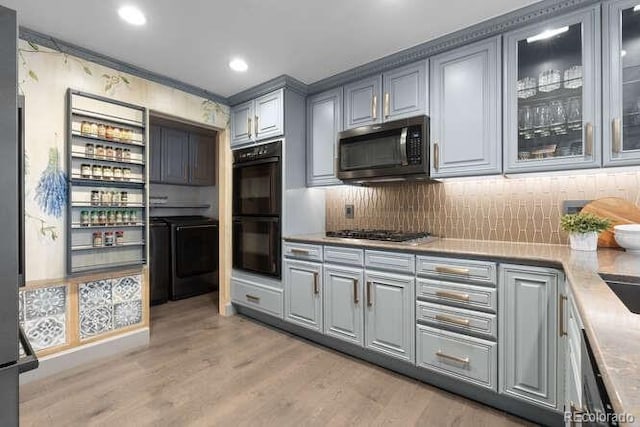 kitchen featuring stainless steel gas stovetop, gray cabinets, light wood-type flooring, double oven, and washing machine and clothes dryer