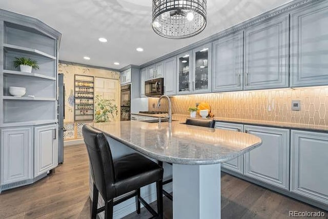 kitchen featuring light stone countertops, dark wood-type flooring, sink, a center island with sink, and gray cabinets