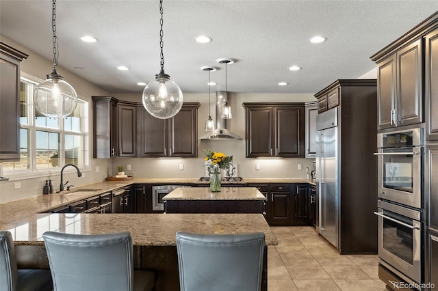 kitchen with pendant lighting, sink, a breakfast bar, a center island, and wall chimney exhaust hood