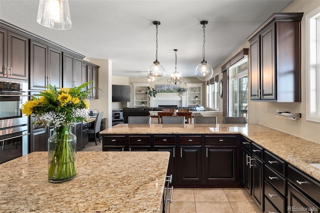 kitchen featuring hanging light fixtures, dark brown cabinetry, light stone countertops, light tile patterned flooring, and stainless steel double oven