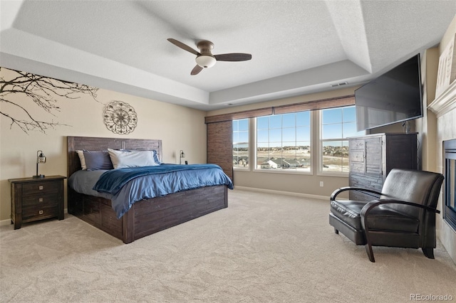 bedroom featuring ceiling fan, light carpet, a textured ceiling, and a tray ceiling