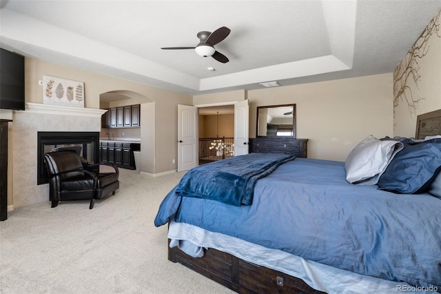 carpeted bedroom with ceiling fan, a raised ceiling, and a tile fireplace