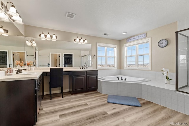 bathroom with independent shower and bath, wood-type flooring, vanity, and a textured ceiling