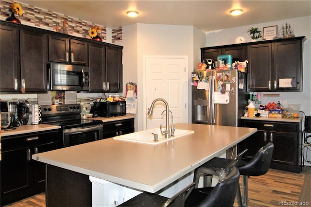 713 Indigo St, Brighton, CO 80603 - kitchen with stainless steel appliances, light wood finished floors, a kitchen breakfast bar, a center island with sink, and light countertops