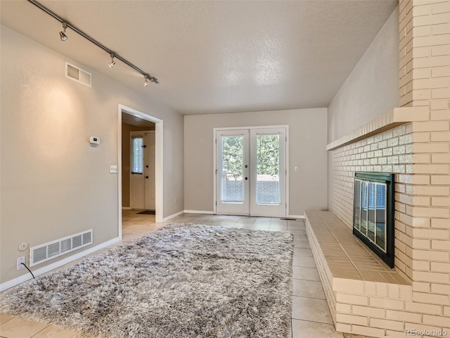 3540 E 5th Ave, Denver, CO 80206 - unfurnished living room featuring rail lighting, light tile patterned flooring, french doors, a brick fireplace, and baseboards