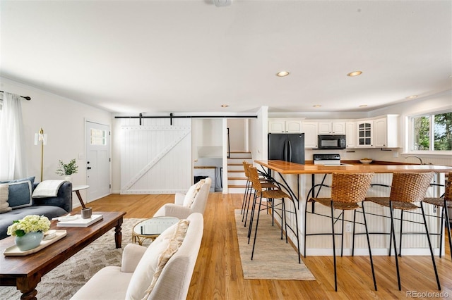 living room featuring a barn door, light wood-style floors, recessed lighting, ornamental molding, and stairway