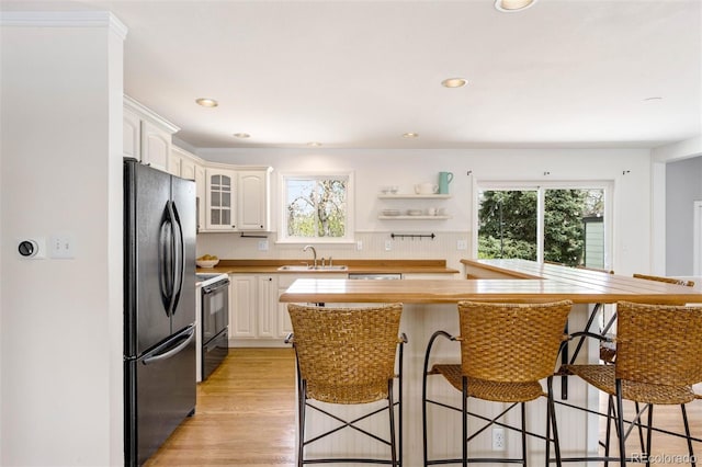 kitchen with freestanding refrigerator, electric range, a breakfast bar area, and white cabinets