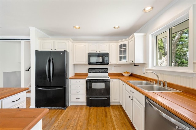 kitchen with tasteful backsplash, light wood-type flooring, a sink, white cabinets, and black appliances