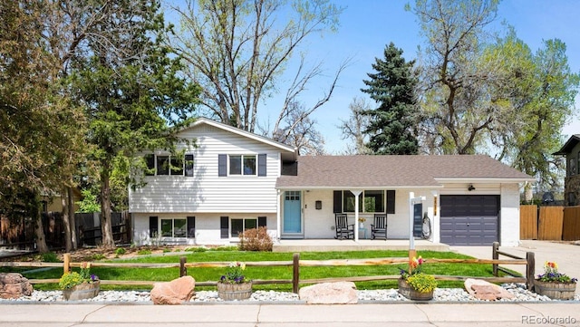 split level home featuring brick siding, a garage, a porch, fence private yard, and driveway