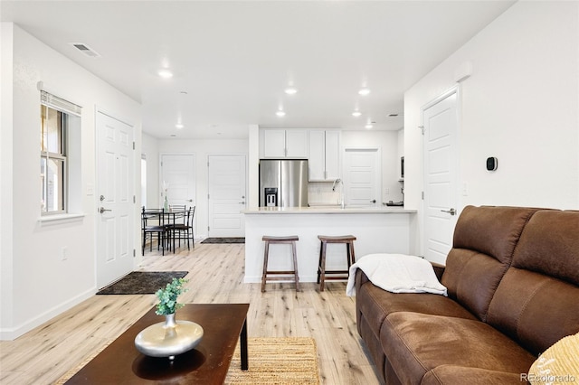 living room featuring baseboards, visible vents, recessed lighting, and light wood-style floors