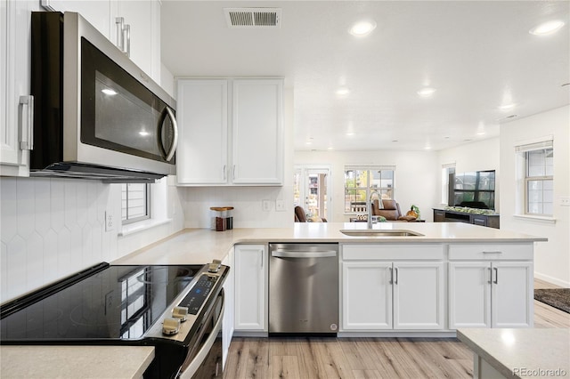 kitchen with light wood finished floors, stainless steel appliances, visible vents, a sink, and white cabinetry