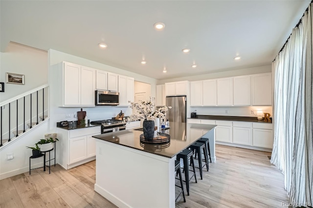 kitchen featuring light wood finished floors, a kitchen bar, dark countertops, stainless steel appliances, and white cabinets