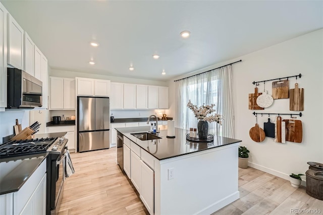 kitchen featuring a sink, dark countertops, stainless steel appliances, white cabinets, and light wood-type flooring