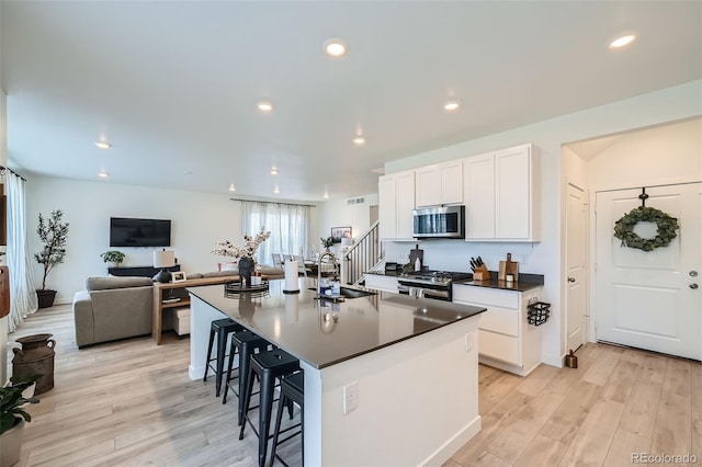 kitchen with light wood-type flooring, dark countertops, appliances with stainless steel finishes, and a sink