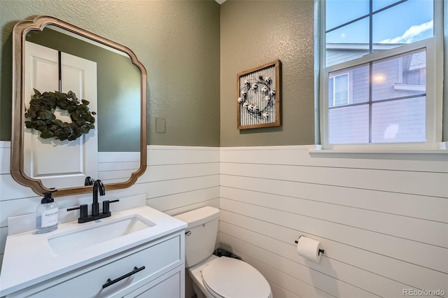 bathroom with vanity, toilet, wainscoting, and a textured wall