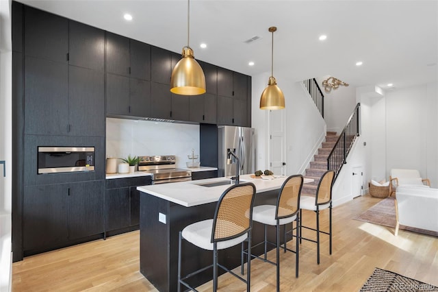 1250 Yates St, Denver, CO 80204 - kitchen with stainless steel appliances, a center island with sink, dark cabinetry, light countertops, and recessed lighting