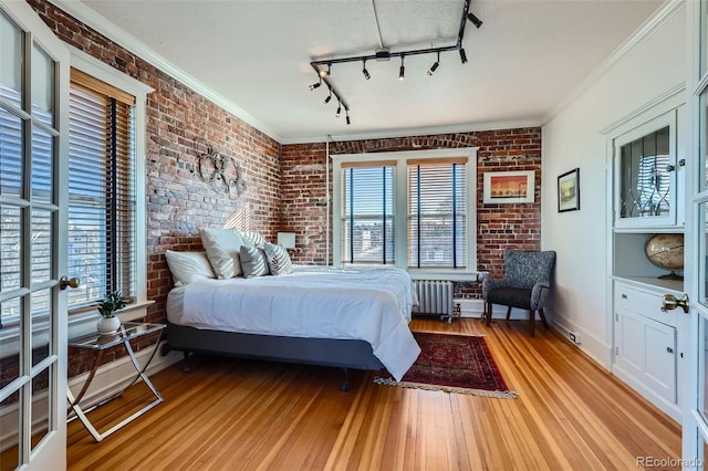 bedroom featuring crown molding, brick wall, radiator heating unit, and light wood-type flooring