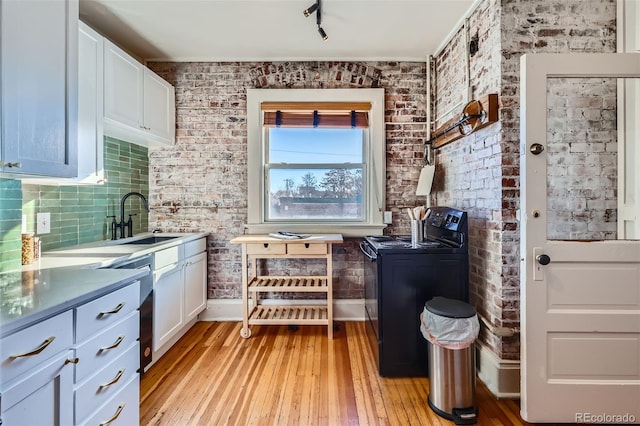 kitchen with brick wall, sink, white cabinets, light hardwood / wood-style floors, and black range with electric stovetop