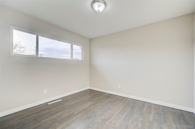 spare room with baseboards, dark wood finished floors, and visible vents