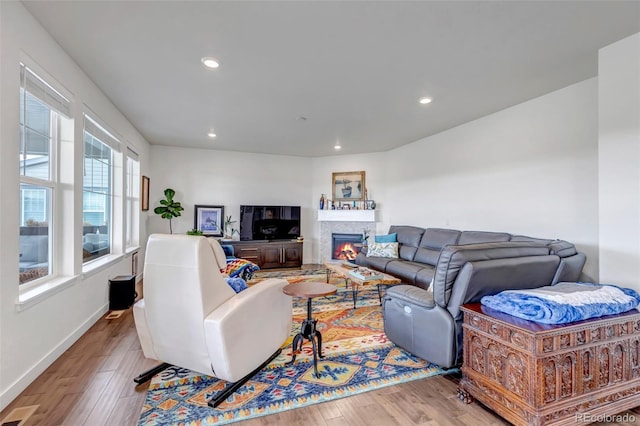 living area with wood finished floors, recessed lighting, a warm lit fireplace, and baseboards