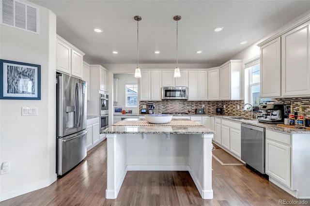kitchen featuring stainless steel appliances, a sink, a center island, tasteful backsplash, and white cabinetry