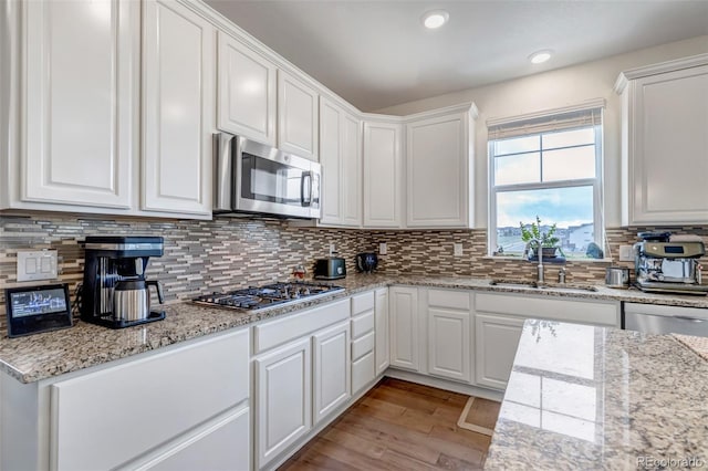 kitchen with appliances with stainless steel finishes, a sink, white cabinetry, wood finished floors, and decorative backsplash