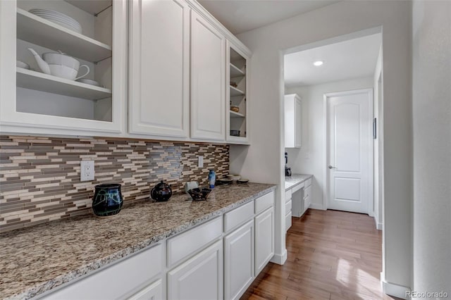 kitchen featuring white cabinets, glass insert cabinets, backsplash, wood finished floors, and light stone counters