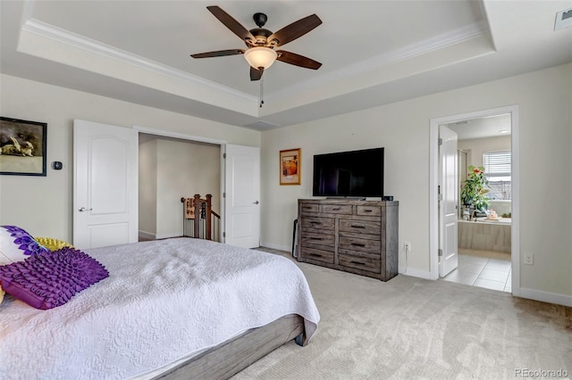 carpeted bedroom featuring a tray ceiling, crown molding, baseboards, and ensuite bathroom