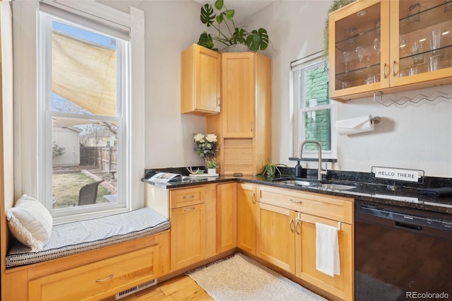 kitchen featuring black dishwasher, a sink, dark stone counters, glass insert cabinets, and light wood-style floors