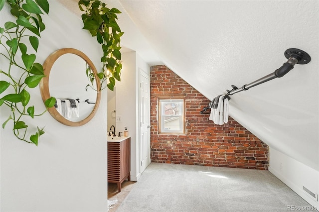additional living space with brick wall, lofted ceiling, carpet flooring, a sink, and a textured ceiling