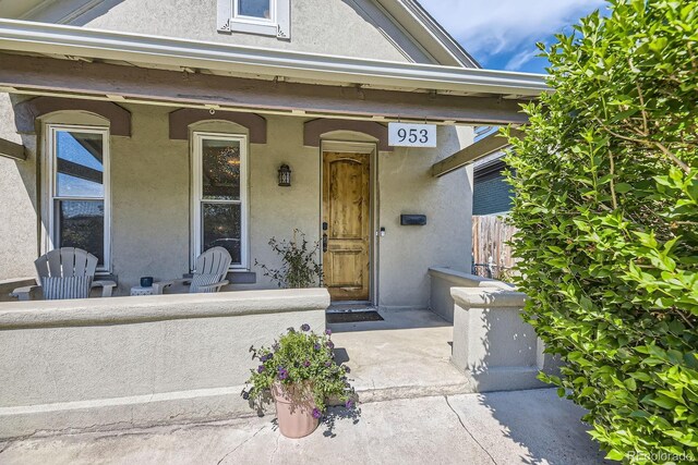 view of exterior entry with stucco siding, a porch, and fence