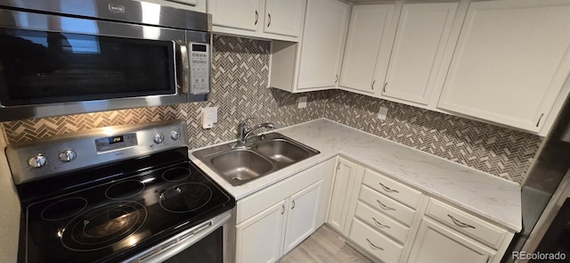 kitchen featuring stainless steel appliances, a sink, white cabinetry, light stone countertops, and tasteful backsplash