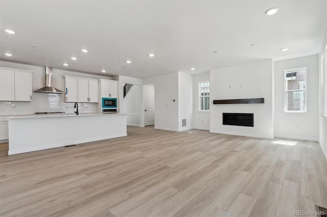 unfurnished living room featuring recessed lighting, light wood-style floors, visible vents, and a glass covered fireplace