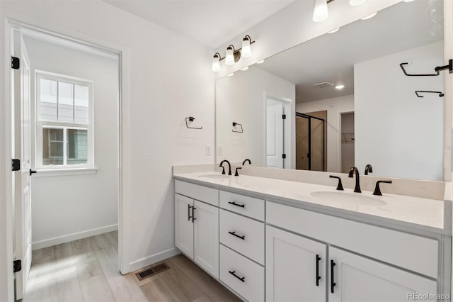 full bath with double vanity, wood finished floors, a stall shower, and a sink
