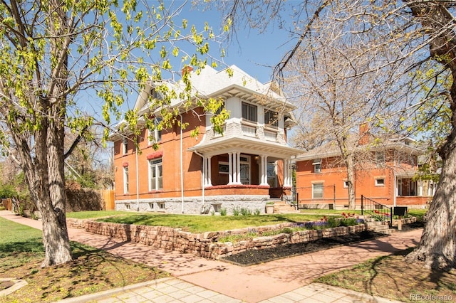 italianate home with a balcony, a front yard, and covered porch