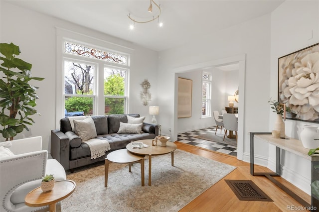living area featuring baseboards, visible vents, a healthy amount of sunlight, and light wood-style floors
