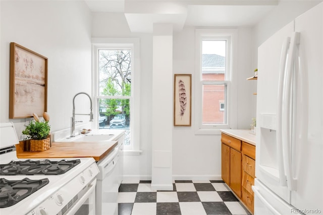 kitchen with a sink, white appliances, light countertops, dark floors, and plenty of natural light