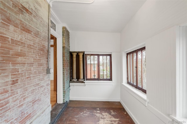 hallway featuring brick wall, baseboards, and wood finished floors