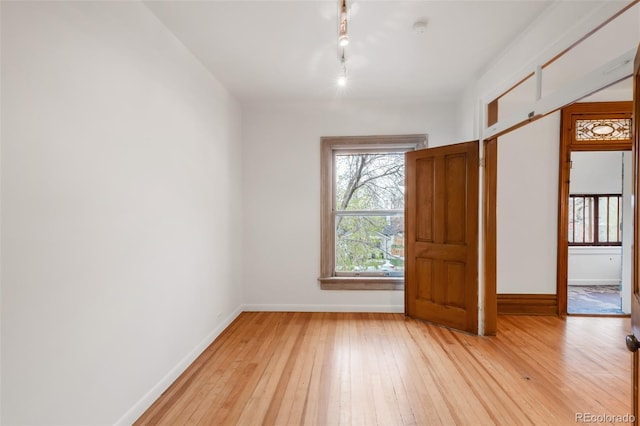 empty room featuring baseboards, light wood-style floors, and track lighting