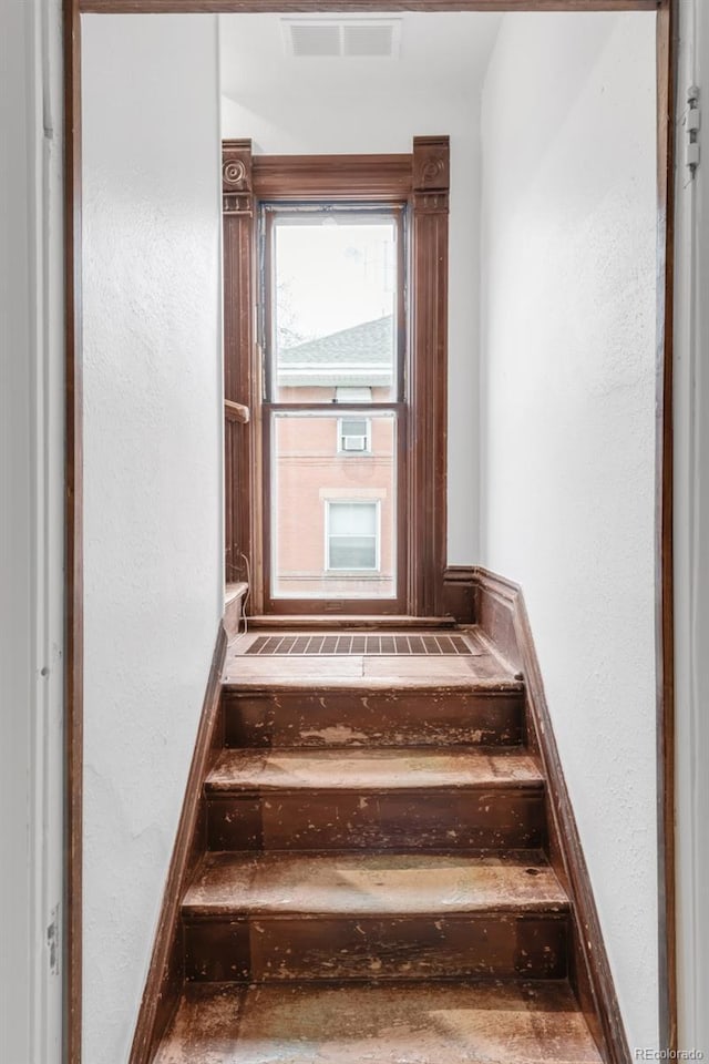 stairs with a textured wall, visible vents, and baseboards