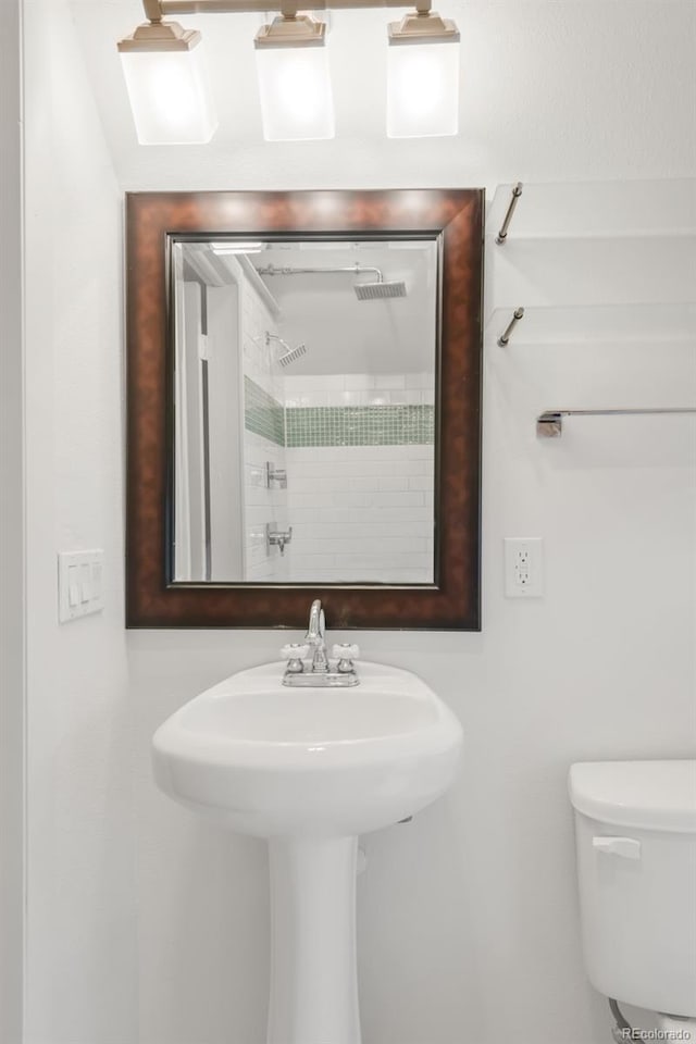 full bathroom with toilet, a tile shower, and a sink