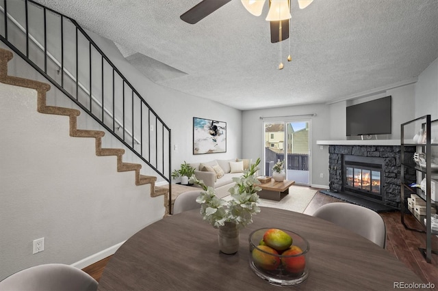 dining space with ceiling fan, a stone fireplace, a textured ceiling, and hardwood / wood-style flooring