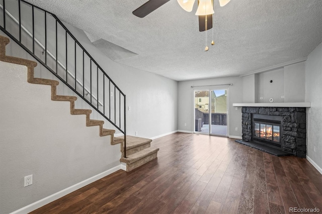 unfurnished living room featuring hardwood / wood-style flooring, ceiling fan, a stone fireplace, and a textured ceiling