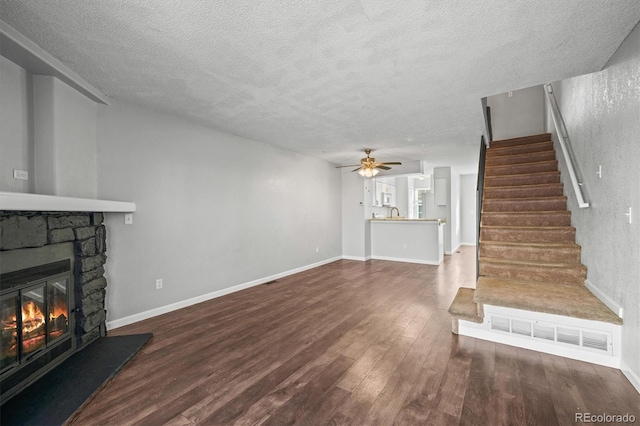 unfurnished living room featuring dark wood-type flooring, ceiling fan, a fireplace, and a textured ceiling