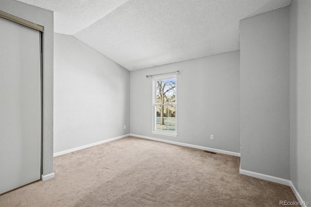 empty room featuring lofted ceiling, carpet flooring, and a textured ceiling