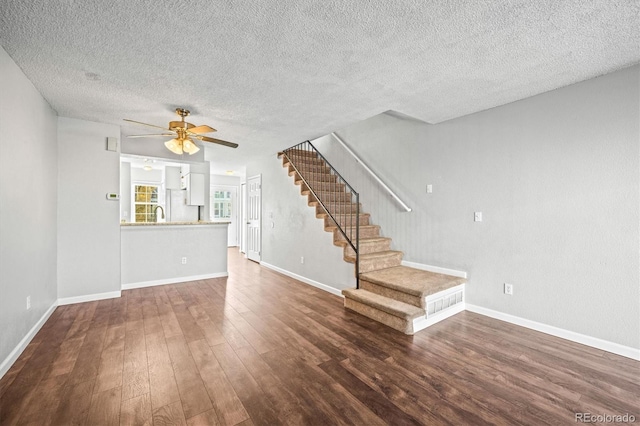 unfurnished living room with a textured ceiling, dark wood-type flooring, and ceiling fan